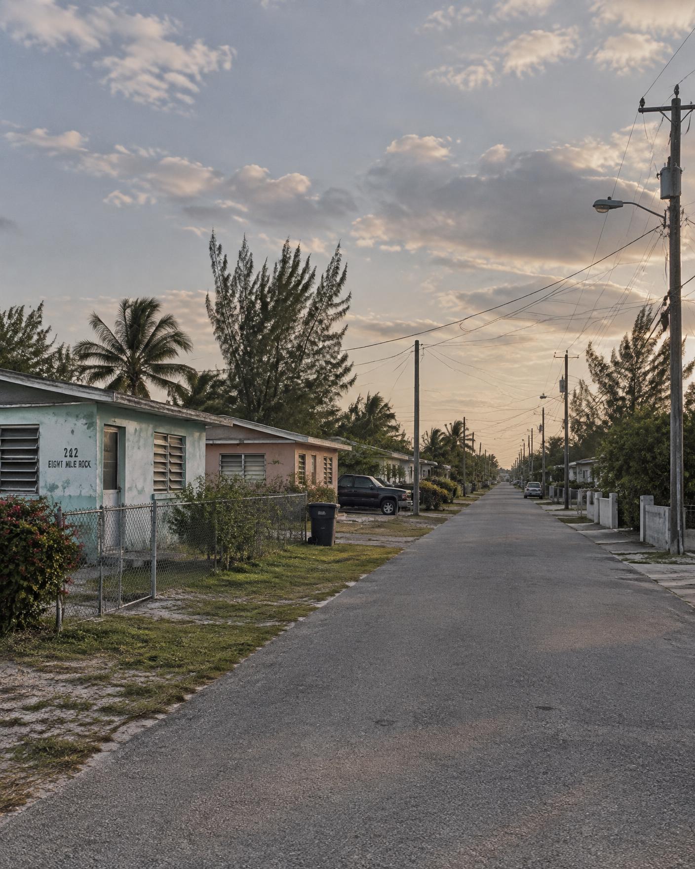 A quiet Grand Bahama residential street in late afternoon light, modest low-rise homes and overhead wires