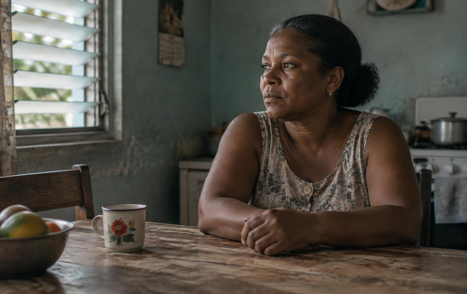 Still: a woman sits alone at a kitchen table in window light